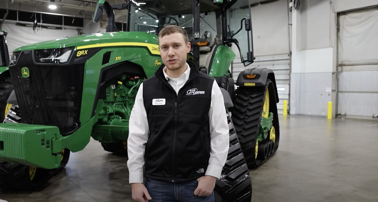 Eddie Tilton stands beside a John Deere 8RX in a garage.